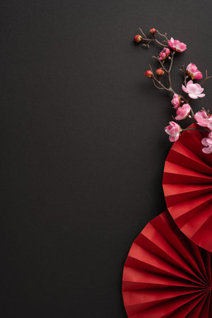 A minimalistic Chinese New Year vertical scene with red folded fans and delicate cherry blossoms on a dark background, symbolizing elegance and traditional celebrationの写真素材