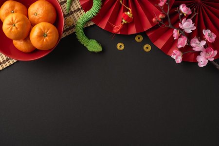 Colorful Chinese New Year arrangement featuring fresh oranges, red fans, cherry blossoms, and traditional gold coins symbolizing prosperity and celebrationの写真素材