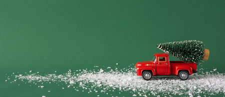 A charming vintage red toy truck carries a miniature Christmas tree across a snowy path. The green background enhances the festive and nostalgic feel of this holiday-themed imageの写真素材