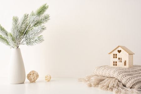 Minimalist side view scandinavian decor featuring a wooden house on a knitted blanket, with snowy pine branches in a vase, creating a peaceful winter ambianceの写真素材