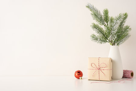 A side view minimalist Scandinavian Christmas setting featuring a pine arrangement in a white vase, gift package with twine, and a red bauble, conveying warmth and simplicityの写真素材