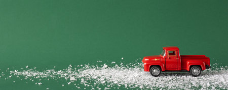 A small red toy truck on a green background, surrounded by scattered snow-like particles, evoking a festive holiday atmosphereの写真素材