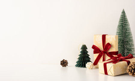 Minimalistic side view scene with Christmas gifts wrapped in brown paper and red ribbons, surrounded by small pine trees on a white backgroundの写真素材