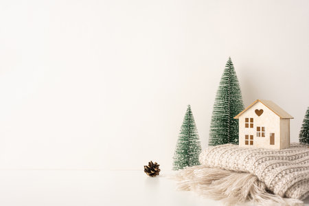 Minimalist side view Scandinavian Christmas scene with a wooden house, pine trees, and knit blanket capturing cozy and serene winter vibesの写真素材