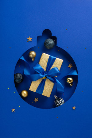Christmas-themed vertical composition featuring a gift box with a blue ribbon surrounded by festive ornaments and golden stars on a blue backgroundの写真素材