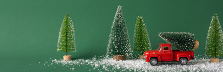 A red toy truck transports a snow-covered Christmas tree through a festive winter landscape with miniature trees. Ideal for holiday themes and winter celebrationsの写真素材
