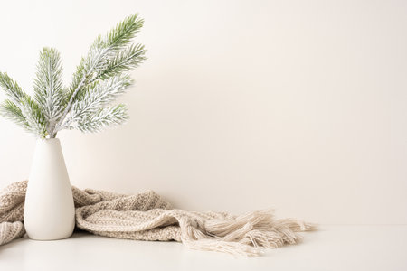 A side view simple and elegant winter scene featuring frosted pine branches in a vase with a cozy knit scarf. The Scandinavian style creates a serene and calming atmosphereの写真素材