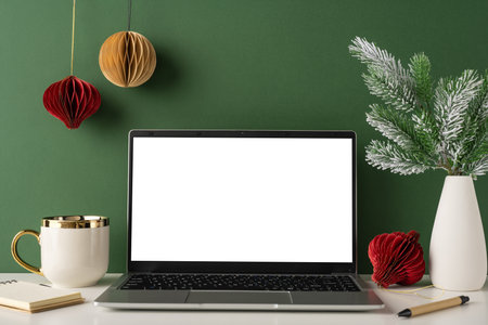 A side view of a clean and elegant workspace featuring a laptop, festive decorations, and a mug in a Scandinavian style settingの写真素材