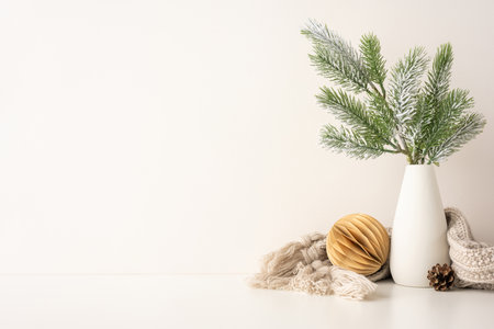A side view simple Scandinavian style setup featuring a white vase with frosted pine branches, a paper ornament, and cozy knitted scarf. Perfect for winter holiday inspiration and minimalist decorの写真素材