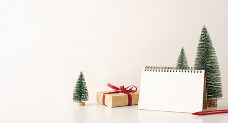A side view minimalistic Scandinavian workspace featuring a blank notebook, decorated with miniature Christmas trees and a giftの写真素材