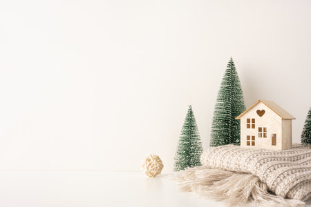 A side view serene Scandinavian style Christmas setup with a wooden house, mini trees, and a cozy textured blanket. It conveys warmth and minimalist holiday decorの写真素材