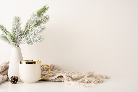 Elegant side view winter scene featuring a frosted pine branch in a vase, a golden-rimmed mug, and a cozy scarf. Perfect for seasonal decoration and warm, inviting feelingsの写真素材