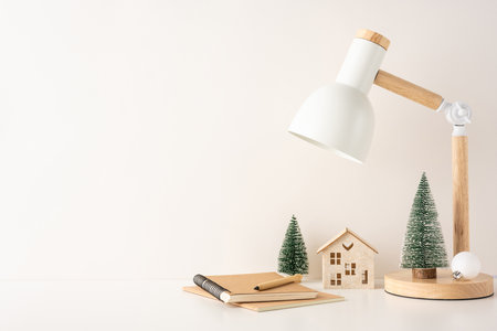 A side view minimalist Scandinavian winter workspace featuring a desk lamp, small pine trees, and a wooden house, creating a cozy and peaceful atmosphereの写真素材