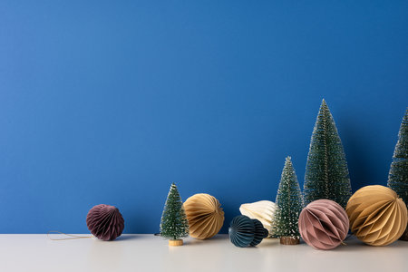 A side view minimalist Scandinavian style winter setup featuring paper ornaments and small artificial trees against a blue wall, creating a cozy festive atmosphereの写真素材