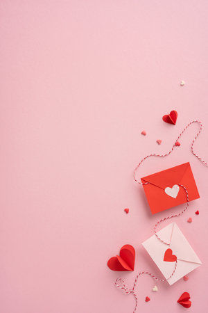 Red and white vertical envelopes with heart cutouts placed on a pink background, symbolizing love and affection. Ideal for Valentine's Day themesの写真素材