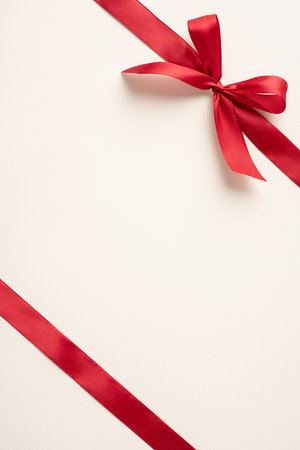 A vertical red ribbon tied into a bow sits against a minimalist cream background, evoking elegance and simplicity. Perfect for holiday themes, celebrations, or gift-wrapping conceptsの写真素材