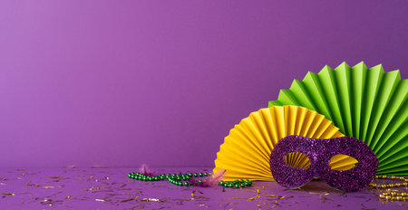 Purple side view background with glittery purple mask, paper fans, green beads, and scattered confettiの写真素材