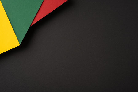 Abstract composition featuring red, green, and yellow paper sheets overlapping on a dark backdrop, creating contrastの写真素材