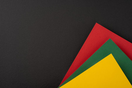 Vibrant colored paper sheets in red, yellow, and green against a plain black backgroundの写真素材