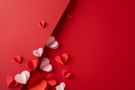 Red and pink paper hearts creatively arranged on a bright red surface, representing love and affection for Valentine's season, suitable for romantic designs or celebration-themed visualsの写真素材