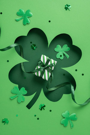 Green vertical shamrocks surround a small gift wrapped with striped paper and ribbon for a festive holiday themeの写真素材