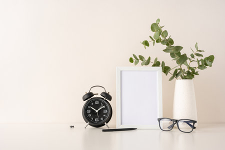 Modern minimalist arrangement featuring a clock, plant, photo frame, and glasses, showing a touch of greenery and simplicity in design on a beige-toned backgroundの写真素材