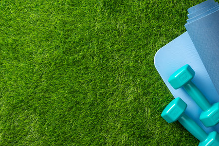 Exercise equipment includes blue dumbbells and a yoga mat positioned on vibrant green grass surfaceの写真素材