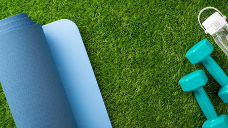 Outdoor fitness setup with yoga mat, dumbbells, and a water bottle on grassの写真素材