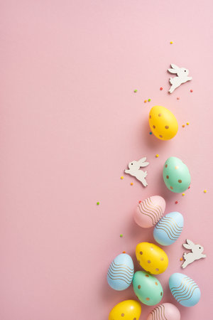 Brightly vertical colored Easter eggs laid out on a pink surface with small wooden bunnies in decorative positions celebrating Easter season fun and creativity in festive adornmentsの写真素材