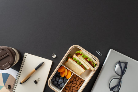 Lunchbox with healthy food, a coffee cup, and accessories on a dark table settingの写真素材