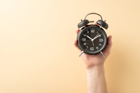 Image showcasing a hand holding a black analog alarm clock with a pastel background