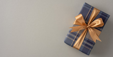 Blue plaid wrapped gift with golden bow placed on beige surface for festive conceptsの写真素材