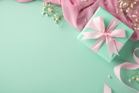 Green gift box adorned with a pink ribbon, surrounded by delicate flowers and fabric accents, creating an elegant and festive atmosphereの写真素材