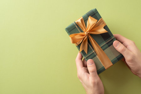 Hands holding a wrapped gift box featuring a plaid pattern with a golden ribbon bowの写真素材