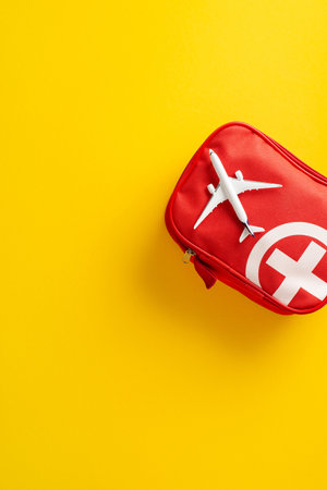 A vertical red first aid kit for travel safety placed beside a airplane small modelの写真素材