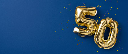 Gold number balloons shaped as fifty, symbolizing celebration, displayed with confetti on blueの写真素材