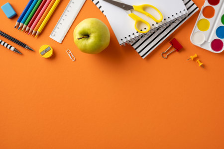 Various school supplies including notebooks, pencils, and an apple arranged on an orange surfaceの写真素材