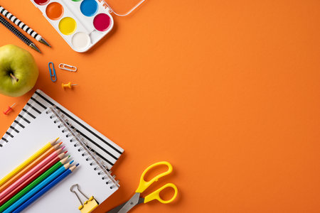 Creative arrangement of school supplies including notebooks, pencils, scissors, apple, and paint against a vibrant orange background, symbolizing education and back-to-school themesの写真素材