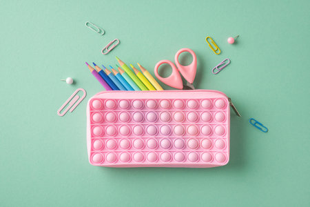 Creative arrangement of a pink pop-it pencil case with vibrant stationery on a pastel surface