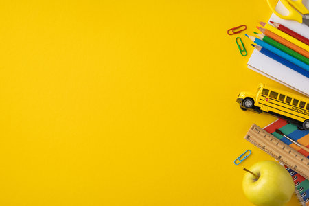 School supplies including books, pencils, and a toy bus on a vivid yellow background