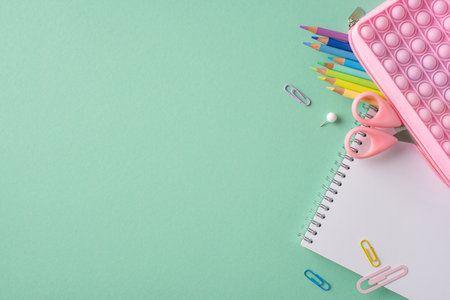 Back-to-school arrangement featuring stationery items such as colored pencils, scissors, and notepads on a minimal green backgroundの写真素材