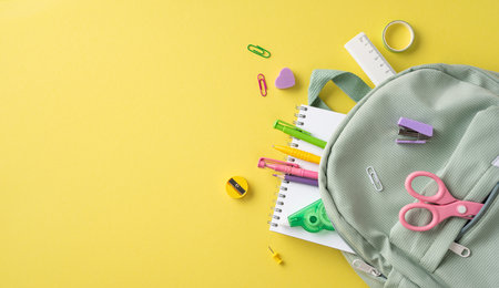 Various colorful school supplies and a green backpack arranged on a bright yellow surface