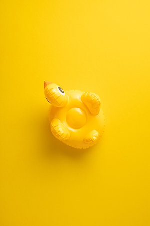 Yellow vertical inflatable duck pool float on a vibrant background creating a cheerful summer vibeの写真素材