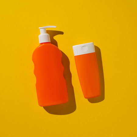 Two square plastic bottles, one with a pump dispenser, on a vibrant yellow backdropの写真素材