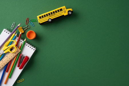 Collection of colorful school stationery placed on a green background with toy school busの写真素材