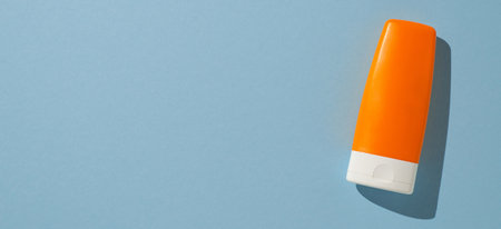 A bright orange sunscreen bottle resting on banner light blue surface with soft shadowsの写真素材