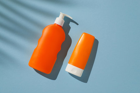 Bright orange skincare bottles placed on a pastel blue surface under warm sunlight shadowsの写真素材
