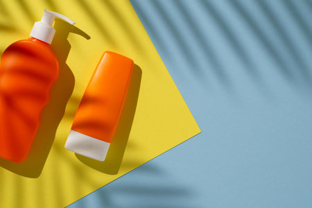 Flat lay of orange sunscreen bottles against yellow and blue background with light shadows, representing skincare and summer essentialsの写真素材