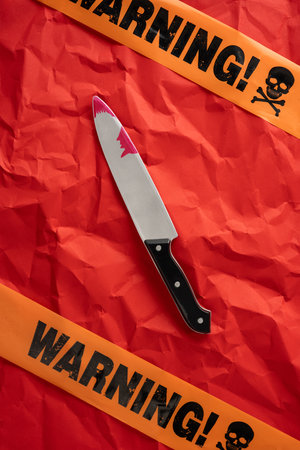 Knife placed on crumpled red vertical surface with Halloween warning tape and decoration
