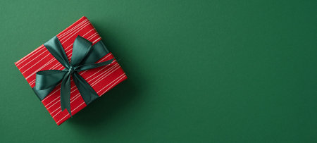 Elegant red gift box with black ribbon sits on green background evoking festivity and celebrationの写真素材